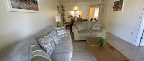 A living room with a sofa, a coffee table, and a dining area in the background.