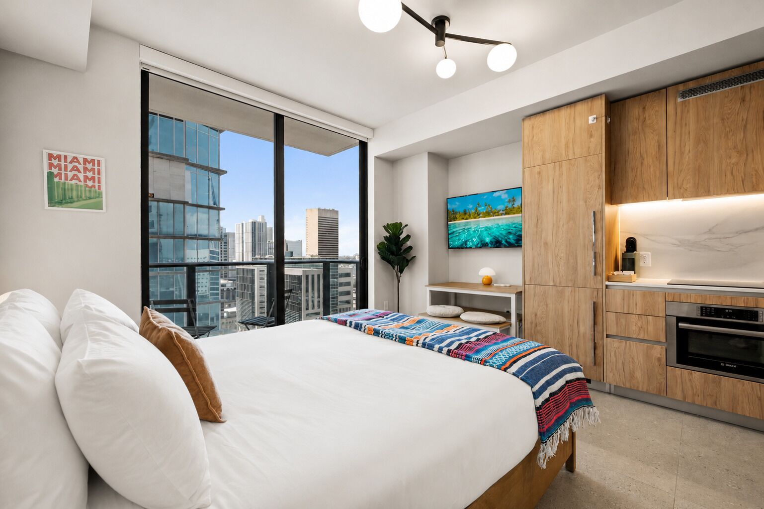 Camera da letto moderna con un letto grande, vista sulla città, angolo cottura e TV a parete.