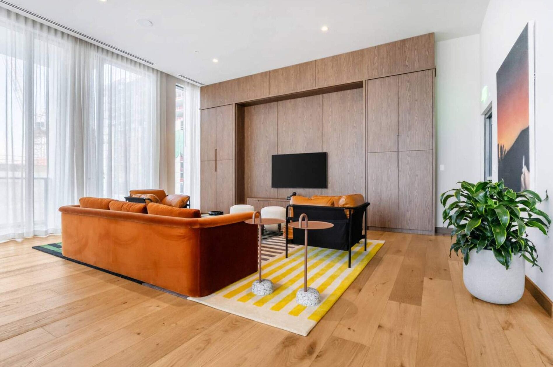 Een moderne woonkamer met houten vloer, een grote bank, een salontafel en een aan de muur bevestigde televisie.
