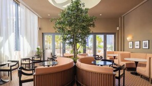 A modern lounge area with round tables and cushioned seating, large windows, and a central tree. - The Crosby Miami Studio by Palermo Home (Miami)