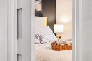 A bedroom with a bed, pillows, a lamp, and a wicker basket. - Shore Cottage | Walk to Beach & Town | Patio Oasis (Belmar)