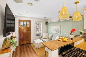 A kitchen with a wooden door, a built-in TV, a checkered ottoman, and a wine rack. - Shore Cottage | Walk to Beach & Town | Patio Oasis (Belmar)