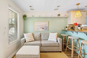 Una sala de estar acogedora con sofá, reposapiés y taburetes de ratán.