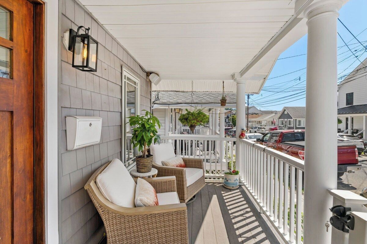 A covered porch with wicker furniture, potted plants, and a white railing.