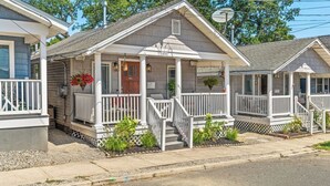 A row of single-story cabins with white railings and a central porch. Each cabin has a small front yard with plants.