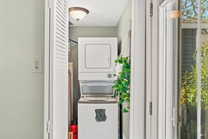 A laundry room with a stacked washer and dryer, a fire extinguisher, and a small plant. - Shore Cottage | Walk to Beach & Town | Patio Oasis (Belmar)