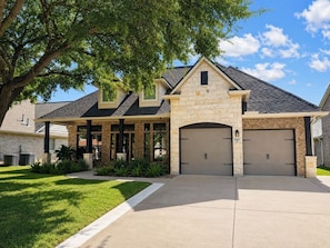 A two-story house with a stone facade, a garage, and a well-maintained lawn. - Settle in and stay awhile at this beautifully furnished luxury home! (New Braunfels)