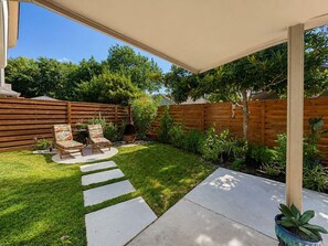 A backyard with a wooden fence, a covered patio area, a stone pathway, and outdoor furniture. - Settle in and stay awhile at this beautifully furnished luxury home! (New Braunfels)