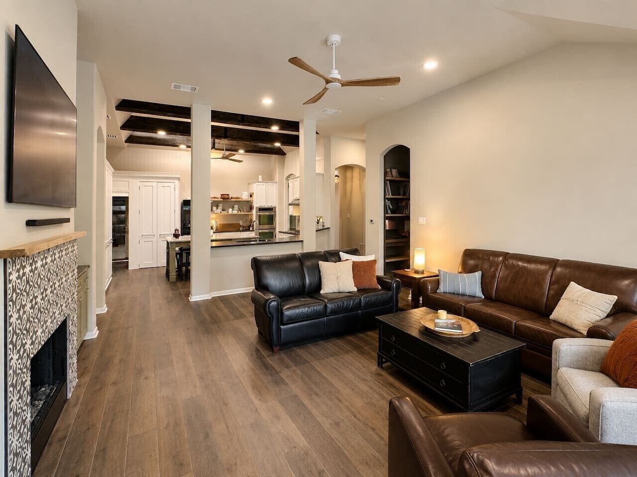 A spacious living room with a fireplace, leather sofas, a coffee table, and a ceiling fan.