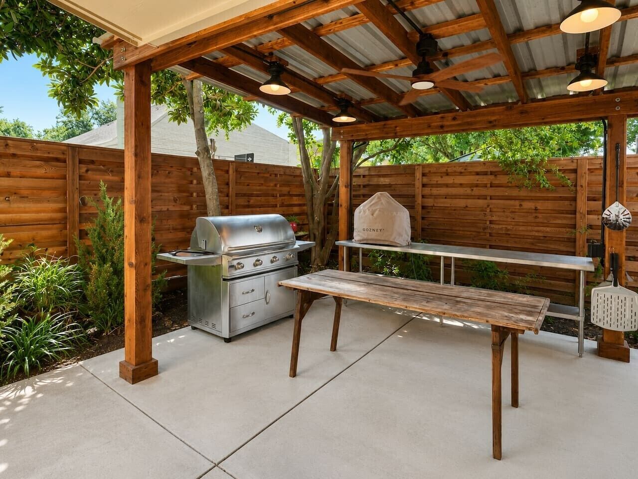 Eine Außenpatio mit Grill, einem Holztisch und einer hängenden Leuchte.