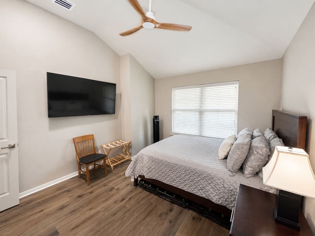 Un dormitorio con cama, una silla, televisor y ventana.