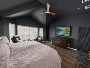 A bedroom with a large bed, a ceiling fan, a TV on the wall, and a window with blinds. - Settle in and stay awhile at this beautifully furnished luxury home! (New Braunfels)