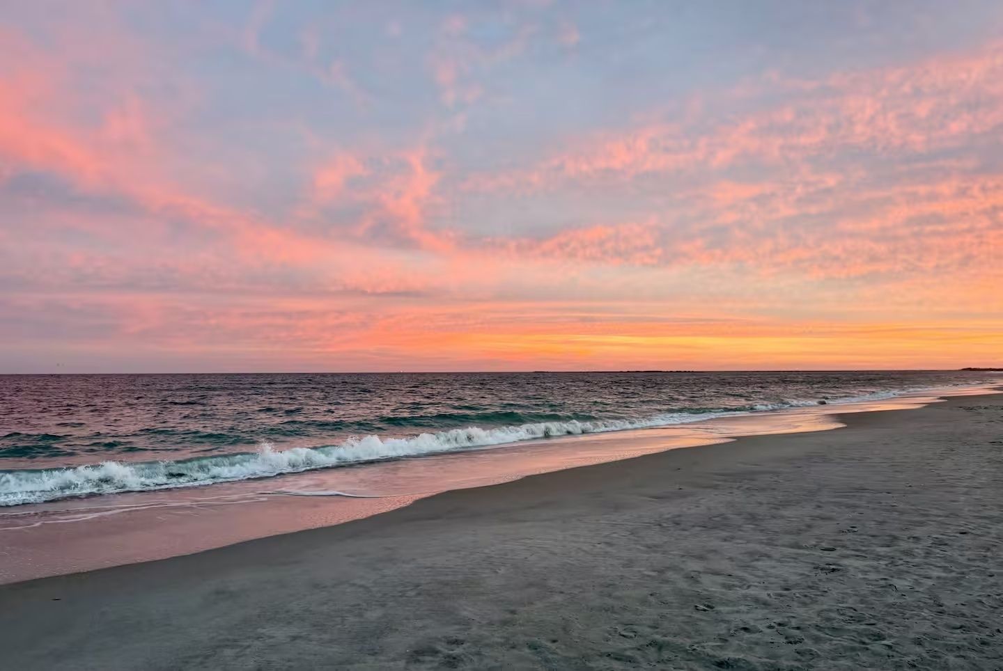 A beach with waves and a sunset sky.