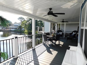 A covered outdoor deck with a view of a lake, a table with chairs, and a ceiling fan. - Ocean Lakes 1576 Spacious 4BR with Hot Tub & Golf Cart (Myrtle Beach)