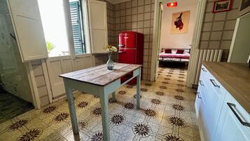 Una cucina compatta con pavimento piastrellato, un tavolo di legno, un frigorifero rosso e un letto sullo sfondo.