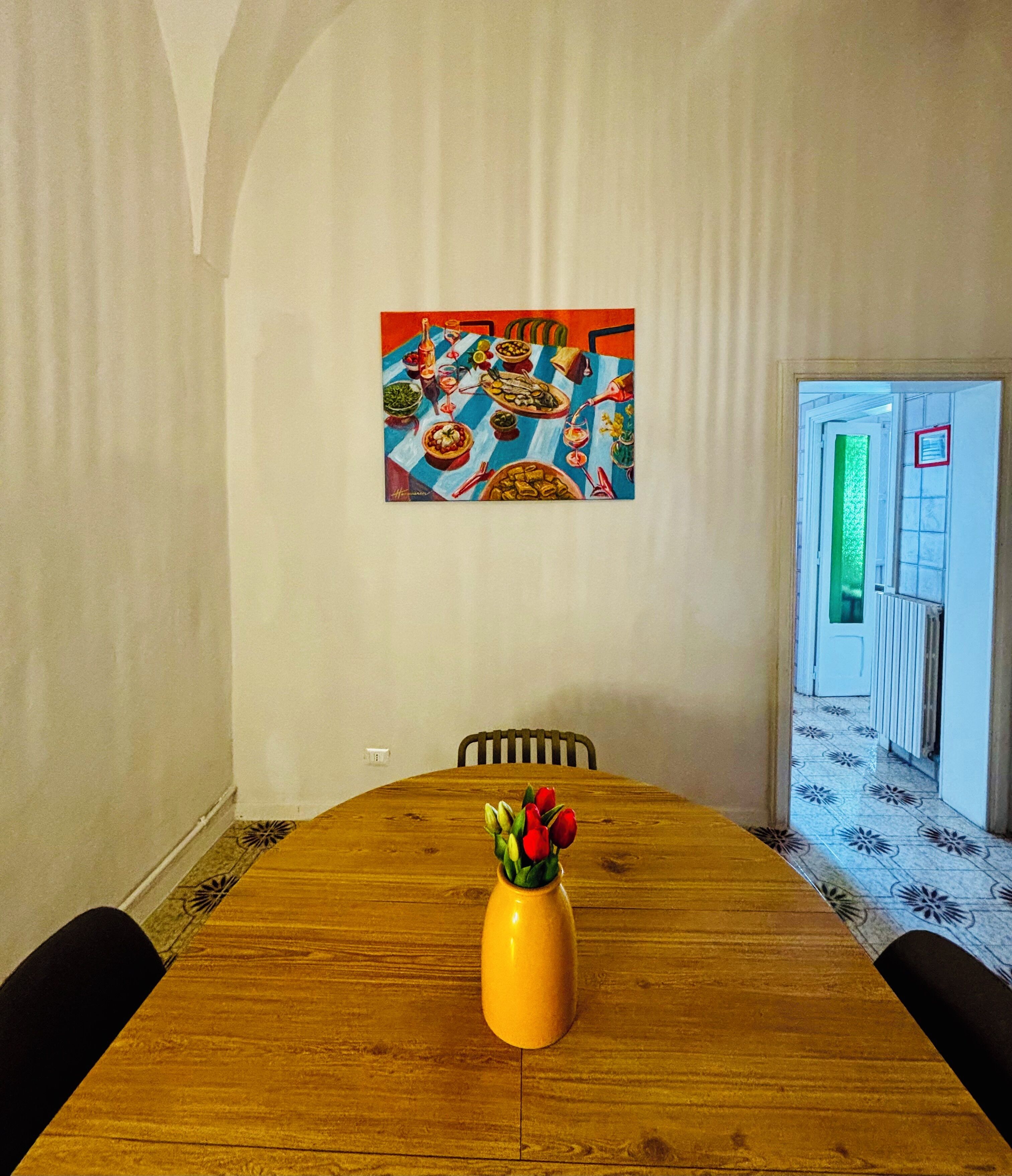 Ein Essbereich mit einem Holztisch, Stühlen, einer Blumenvase und einem farbenfrohen Gemälde an der Wand.