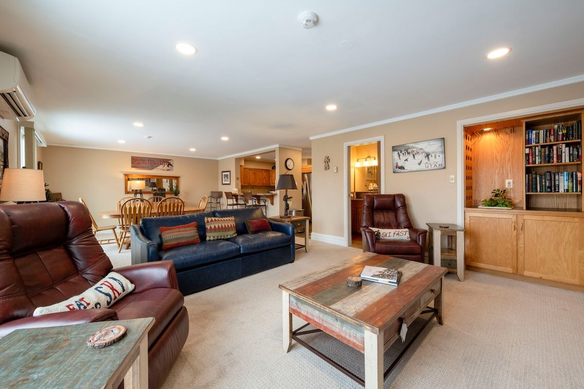 A spacious living room with a leather sofa, a coffee table, and a bookshelf.