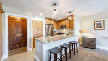 Una cocina con armarios de madera, un refrigerador de acero inoxidable, un microondas y una isla de encimera de granito con taburetes de bar.