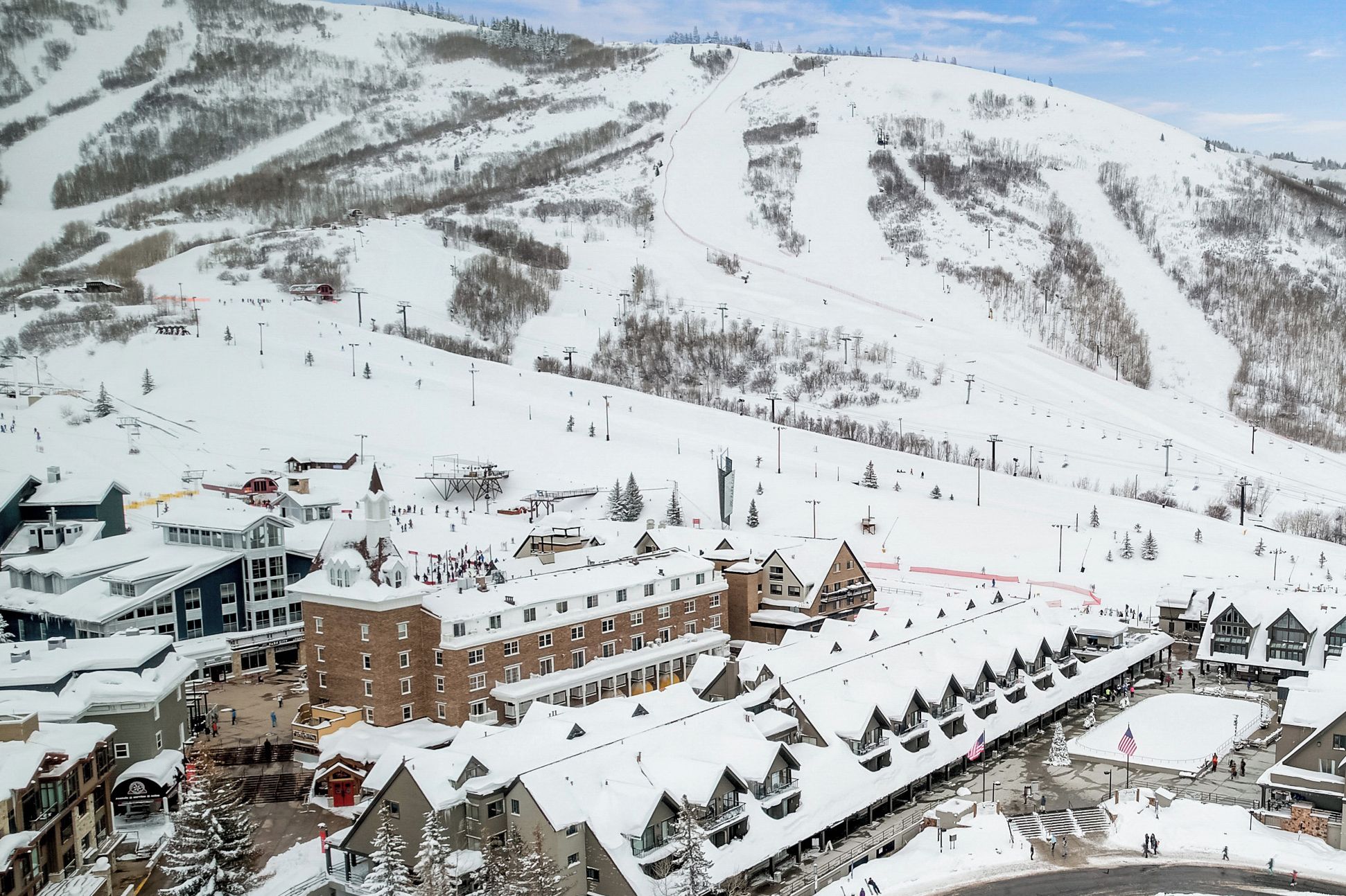 A snow-covered ski resort with buildings, a ski lift, and a mountain backdrop.