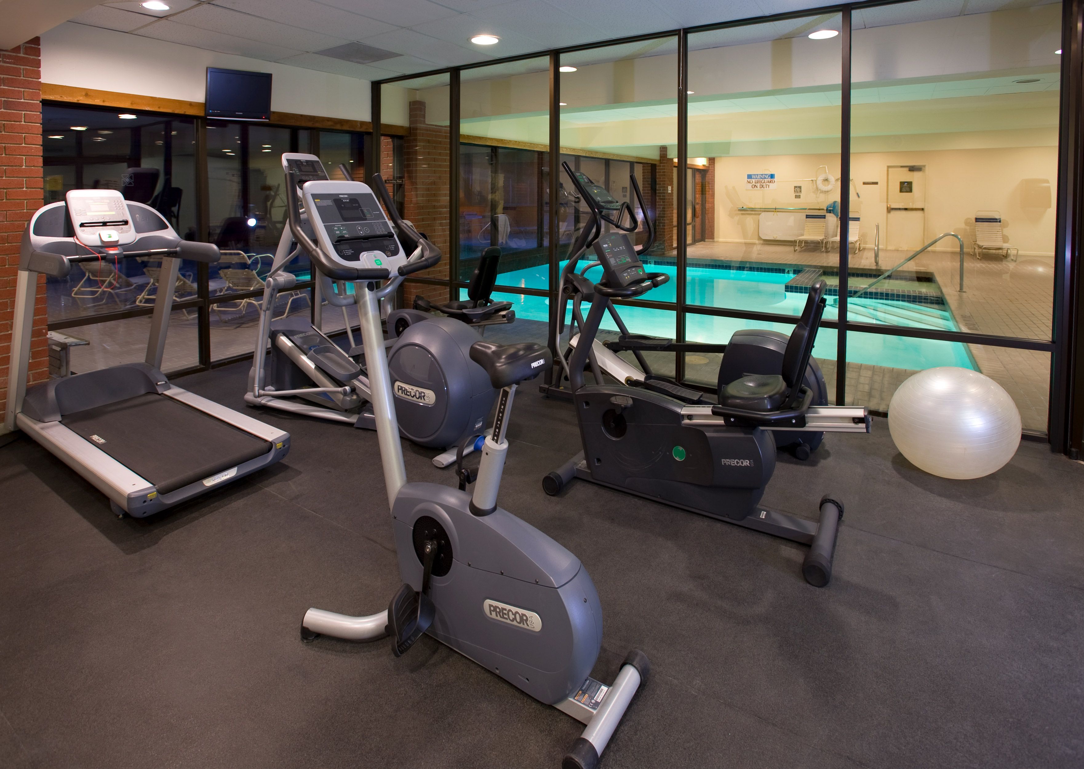 A gym with treadmills, elliptical machines, and a pool area visible through glass walls.
