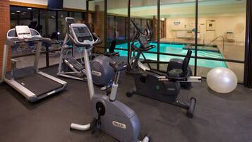 A gym with treadmills, elliptical machines, and a pool area visible through glass walls.