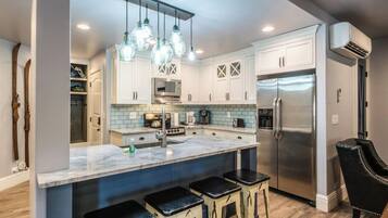 A modern kitchen with white cabinets, a stainless steel refrigerator, and a marble island with bar stools.