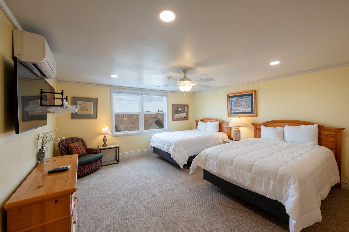 A bedroom with two beds, a ceiling fan, a window, and a bedside table with a lamp.