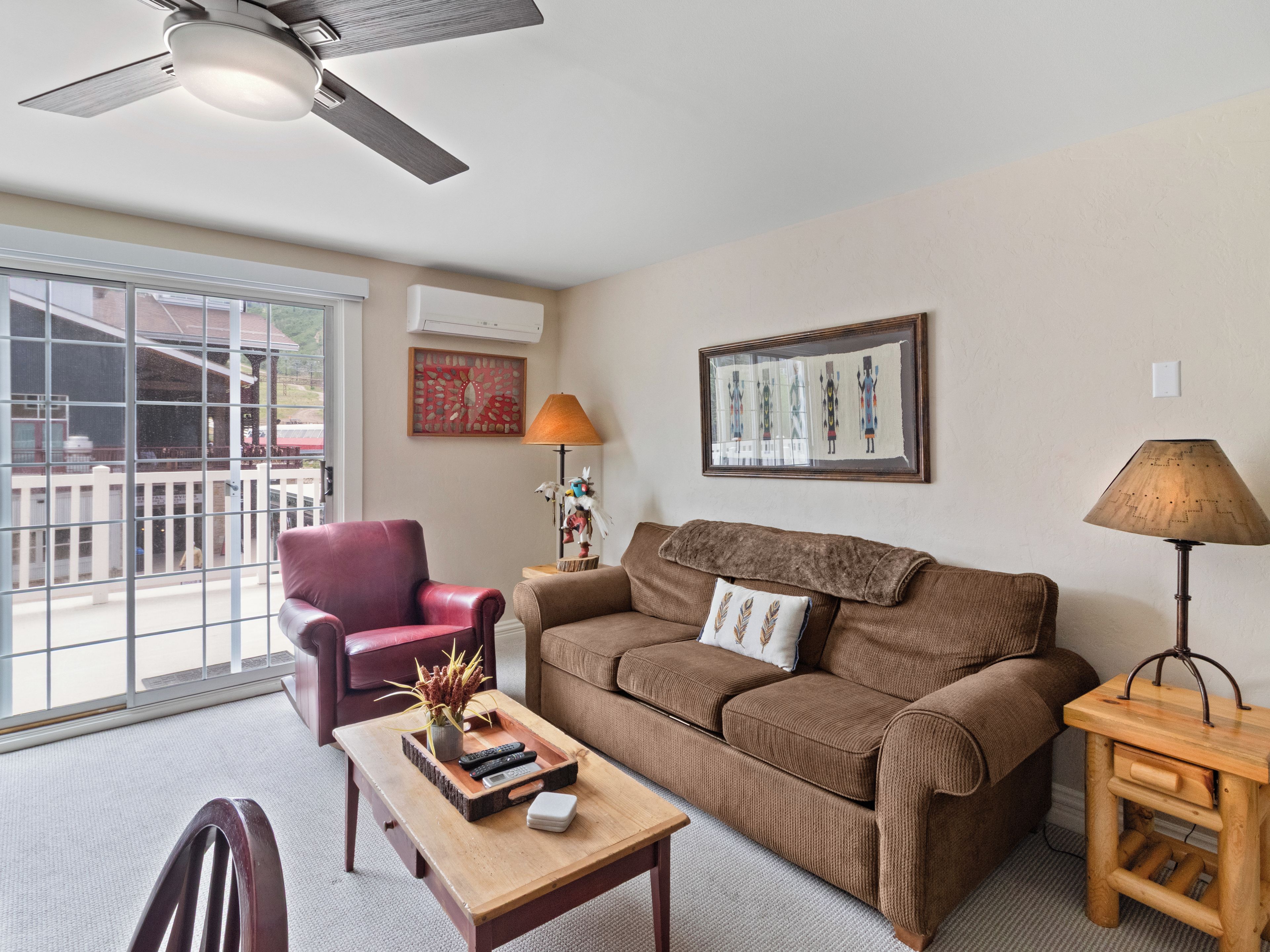 A living room with a brown sofa, a red chair, a wooden coffee table, and a ceiling fan.