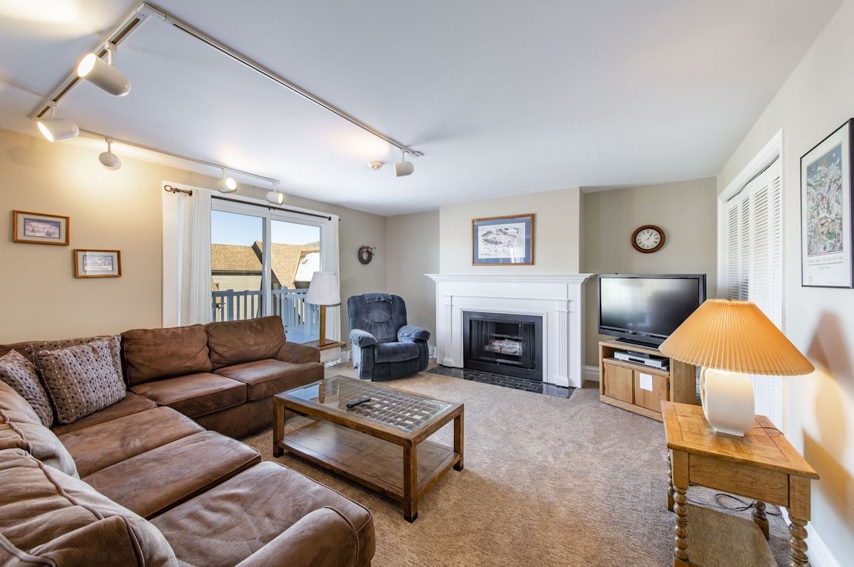 A living room with a sofa, armchair, fireplace, television, and a lamp.