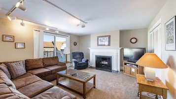 A living room with a sofa, armchair, fireplace, television, and a lamp.