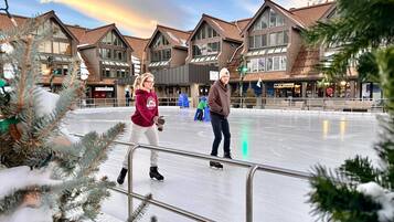 Une patinoire en plein air, entourée de bâtiments au style architectural moderne et dotée d’une barrière métallique.