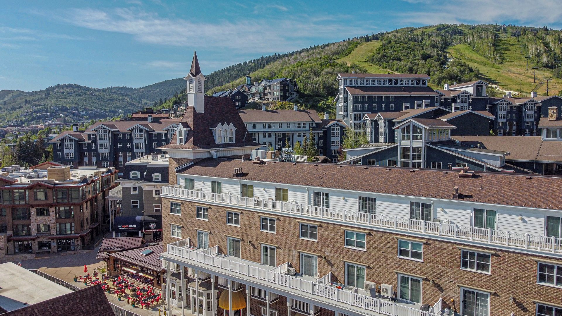 A multi-story building with a prominent church steeple, a variety of residential units, and a commercial area with outdoor seating.