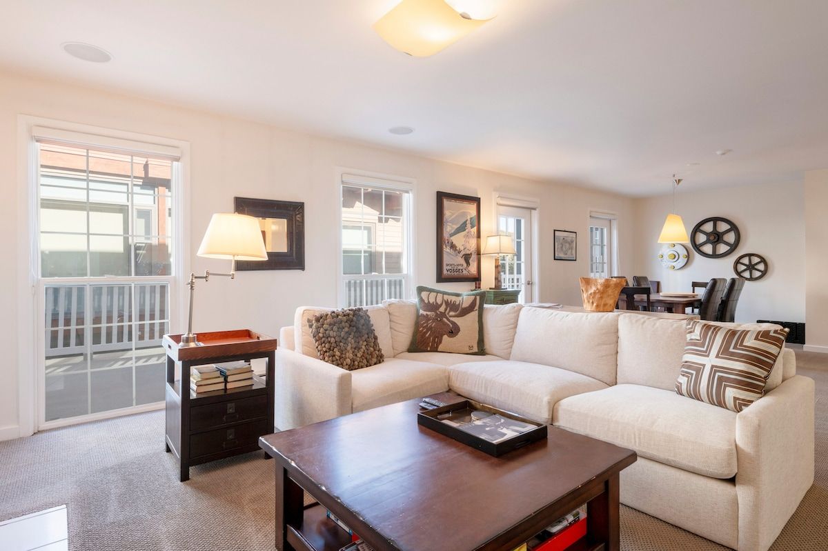 A living room with a sectional sofa, a coffee table, a side table with books, and a lamp.