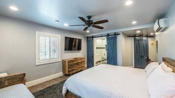 A bedroom with a large bed, a ceiling fan, a TV, and a wardrobe.