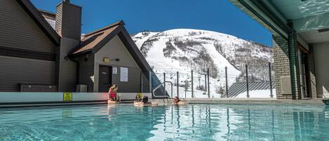 Una piscina con agua cristalina, una montaña al fondo y un edificio con un telesilla.