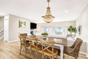 A modern kitchen with a dining area, wooden chairs, a chandelier, and large windows. - North Shore Retreat | Beachfront • Pool • Walkable (South Haven)
