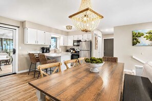 A modern kitchen with white cabinets, a wooden dining table, and a chandelier. - North Shore Retreat | Beachfront • Pool • Walkable (South Haven)