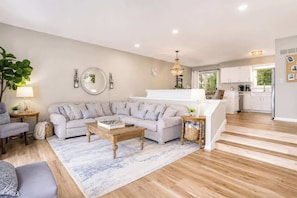 A modern living room with a sectional sofa, a coffee table, and a dining area with a kitchen in the background. - North Shore Retreat | Beachfront • Pool • Walkable (South Haven)