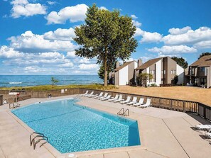 A swimming pool with lounge chairs, a wooden deck, and a view of the ocean. - North Shore Retreat | Beachfront • Pool • Walkable (South Haven)