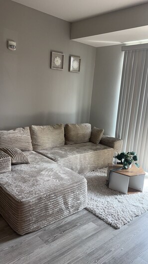 A modern living room with a sectional sofa, a small side table, and a large window with blinds.