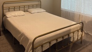 Un letto singolo con struttura in metallo e biancheria da letto bianca in una stanza dalle pareti color beige e tappeto.