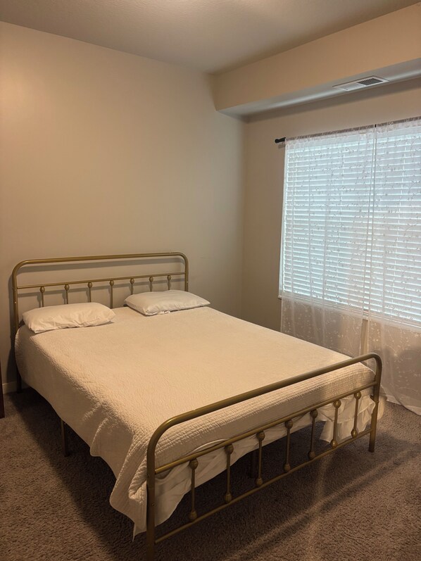 A single bed with a metal frame and white bedding in a room with beige walls and carpet.