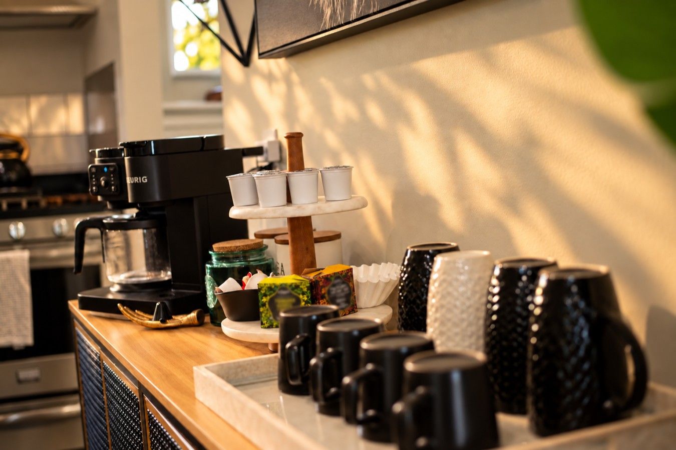 A coffee station with a coffee machine, a tiered dispenser of cups, and a variety of mugs and containers on a wooden counter.