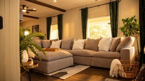 A living room with a sectional sofa, a ceiling fan, and a large window with curtains.