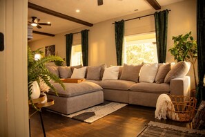 A living room with a sectional sofa, a ceiling fan, and a large window with curtains. - The Moody Modern*2KING beds*2bath*Walkable* (Albany)