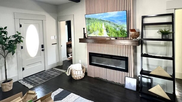 Ein modernes Wohnzimmer mit einem flachbildfernseher an einer Holzwand, einem Kamin, einem Deckenventilator und einer schwarzen Regaleinheit.