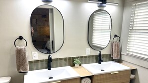 Ein Badezimmer mit zwei Waschbecken, einem Spiegel, Handtuchhaltern und einer Toilette.