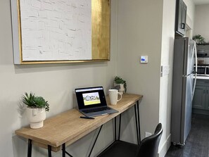 A kitchen with a laptop on a wooden table, two potted plants, a white mug, and a refrigerator.