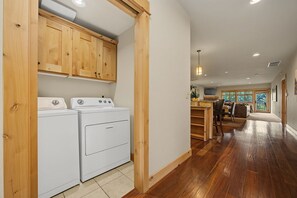 A laundry area with a washing machine and dryer, wooden cabinets, and a kitchen area with a dining table and chairs. - McNeil Point Condo 304 at South Grand Lodge | Spacious 3BR with Best Direct Mt. Hood View (Government Camp)