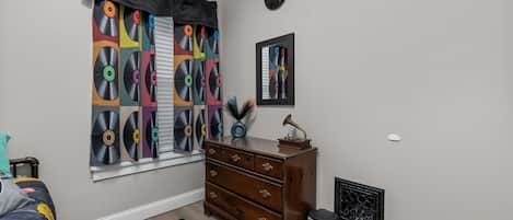 Un dormitorio con una ventana cubierta por una cortina con estampado de disco de vinilo, un aparador, un radiador y un reloj en la pared.